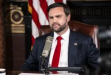 A news-style image of JD Vance speaking at a podium, with subtle U.S., Israeli, and Iranian flags in the background to represent international diplomacy.