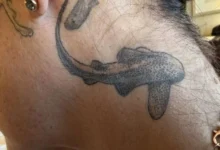 Emily Morrison displaying her shark-themed tattoos while standing near a large aquarium, celebrating her Guinness World Record for the most shark tattoos on a woman.