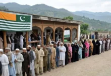 Voters queue outside a polling station during the 2026 Azad Kashmir general elections in Mirpur Division as security personnel monitor the voting process.