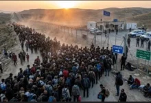 Migrants walking toward a European border crossing as security officials monitor the area