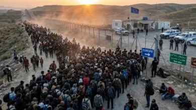 Migrants walking toward a European border crossing as security officials monitor the area